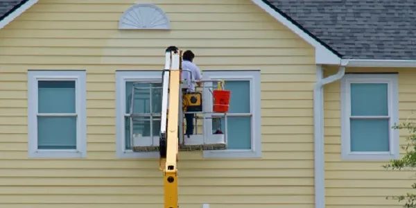 A Painter on a lift painting the siding on a yellow house.