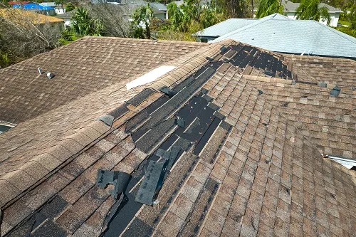 Shingles that have flown off a brown roof.